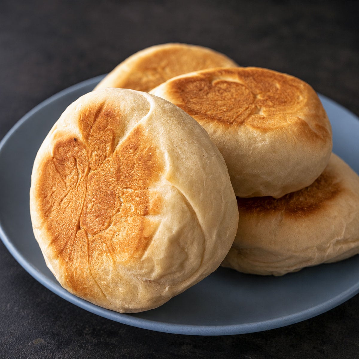 Homemade English muffins stacked on a blue plate with golden tops and a soft, fluffy texture, ready for breakfast or brunch.