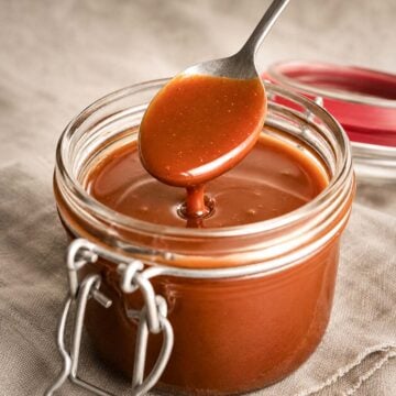 Easy Homemade Salted Caramel Sauce dripping from a spoon into a glass jar, with smooth glossy texture