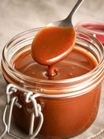 Easy Homemade Salted Caramel Sauce dripping from a spoon into a glass jar, with smooth glossy texture