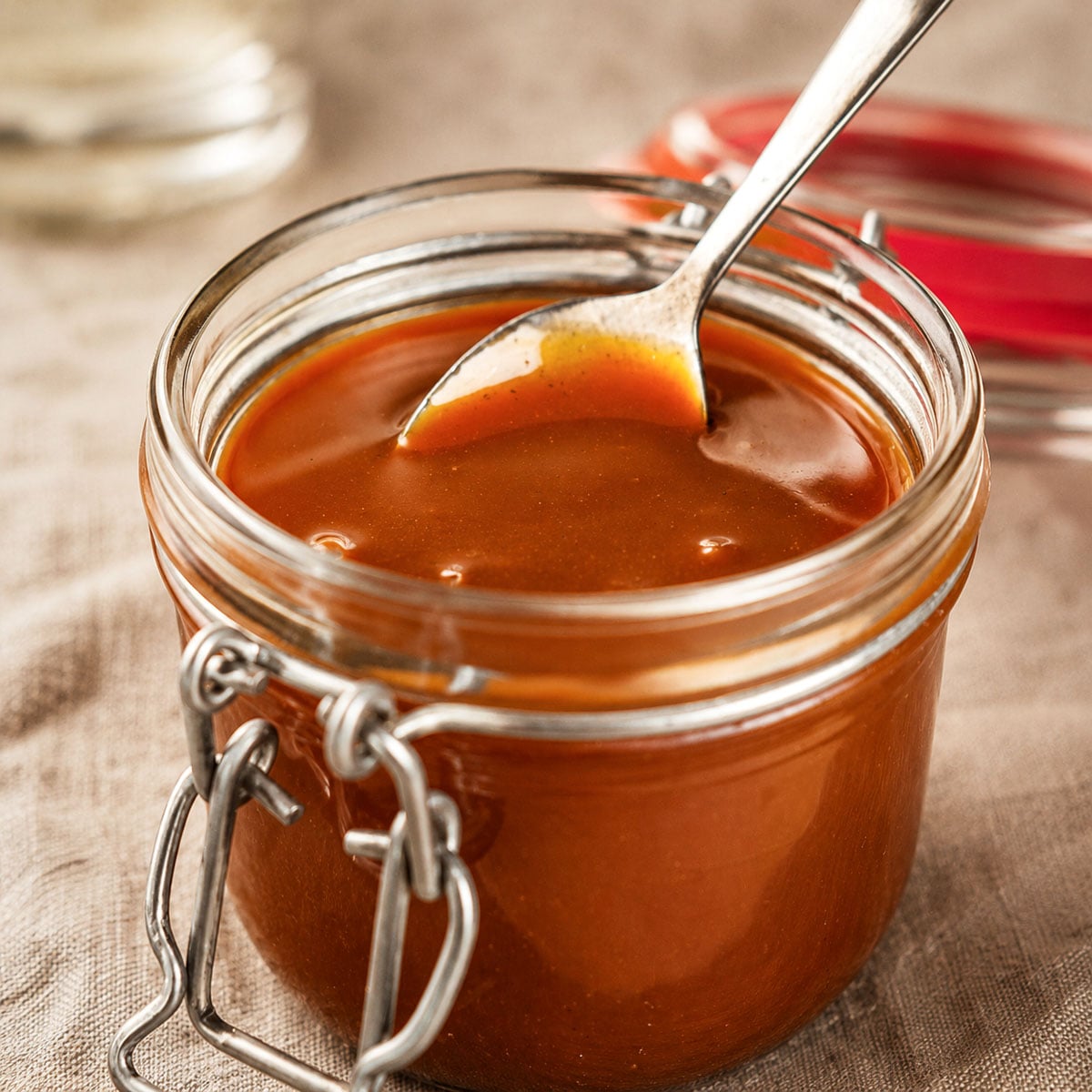 Easy Homemade Salted Caramel Sauce in a glass jar with a spoon, featuring rich glossy caramel