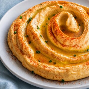 Creamy hummus without tahini swirled with olive oil, paprika, and chives on a plate