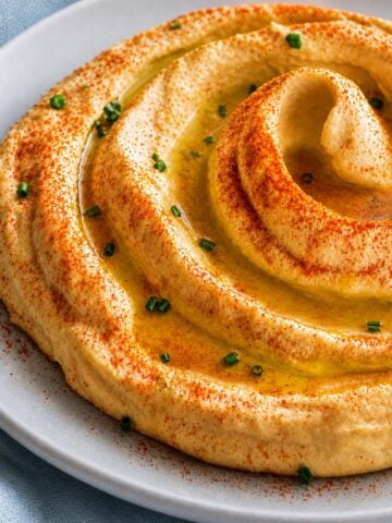 Creamy hummus without tahini swirled with olive oil, paprika, and chives on a plate
