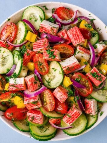 Imitation crab salad without mayo with cucumber, cherry tomatoes, red onion, and fresh herbs in a light lemon dressing.