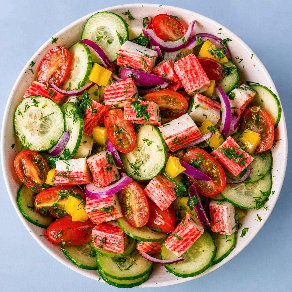 Imitation crab salad without mayo with cucumber, cherry tomatoes, red onion, and fresh herbs in a light lemon dressing.