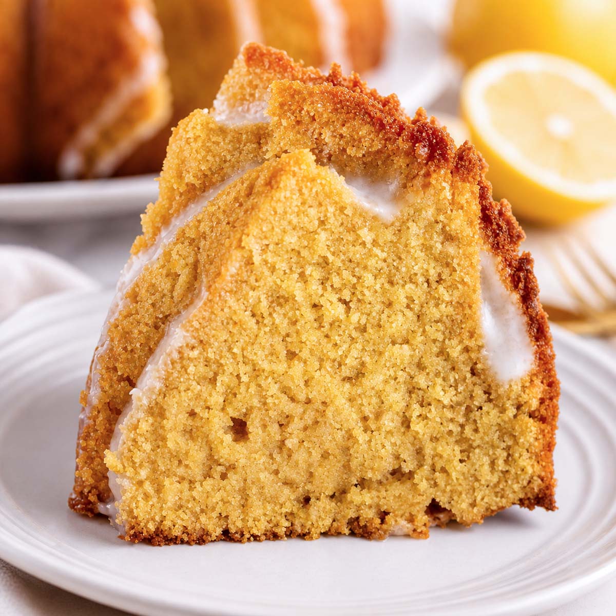 slice of lemon Bundt cake with glaze, soft moist crumb and golden edges on a white plate