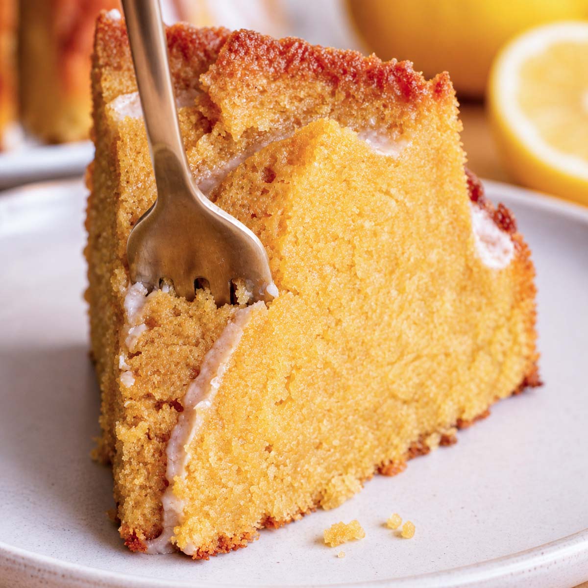slice of lemon Bundt cake with glaze and fork, moist soft crumb with golden crust on a white plate
