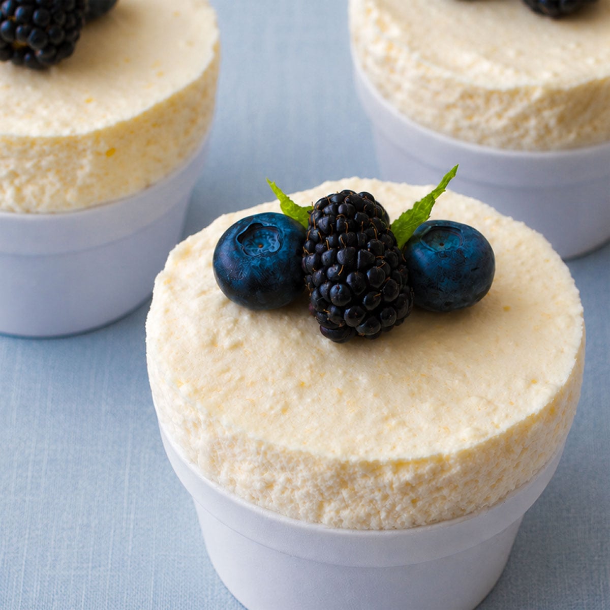 Close-up of a chilled lemon soufflé in a white ramekin topped with blueberries, blackberries, and mint