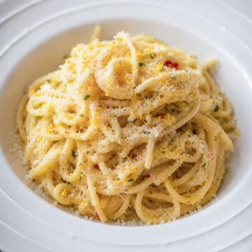 Close up Creamy lemon garlic spaghetti topped with Parmesan cheese in a white bowl, featuring a silky garlic butter sauce and fresh lemon flavor.
