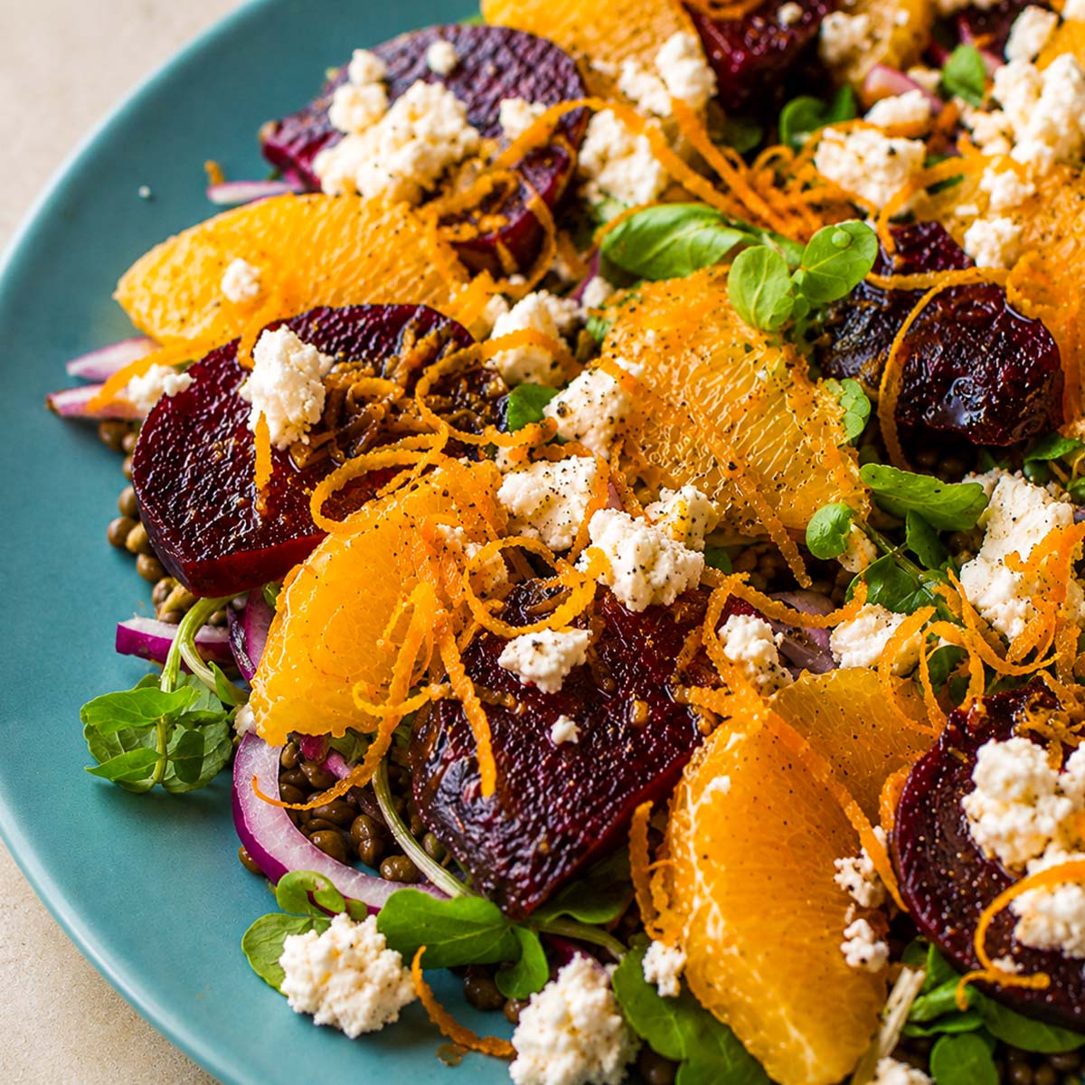Close up Lentil salad with orange dressing and feta topped with roasted beets, citrus segments, and fresh herbs