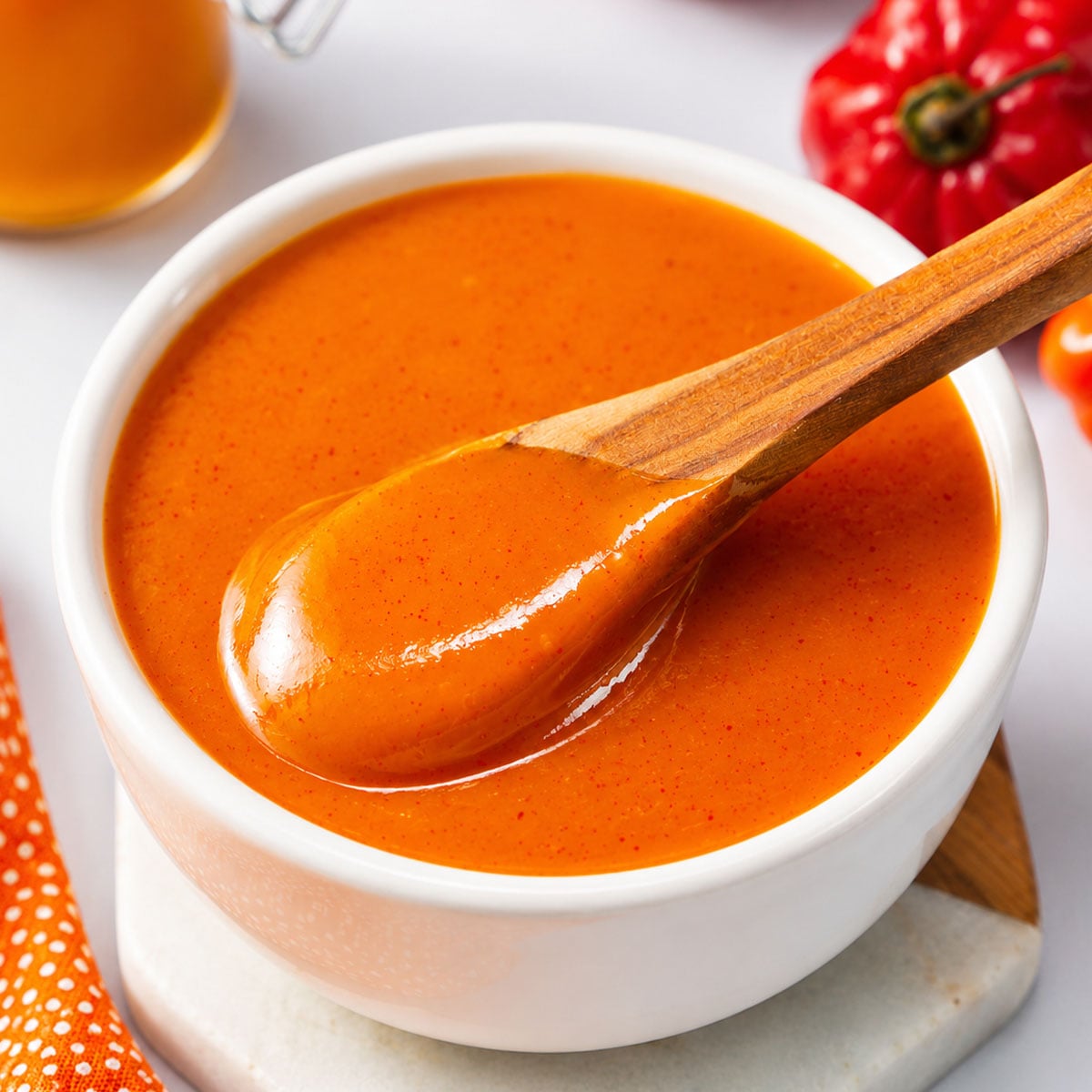 Close up creamy mango habanero hot sauce in a white bowl with a wooden spoon,