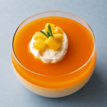 Creamy mango pudding cup topped with whipped cream, fresh mango pieces, and mint