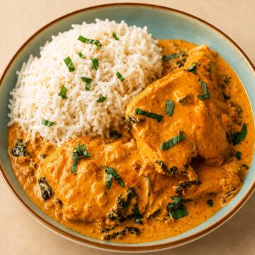 Close up Creamy Marry Me Chicken served with fluffy white rice in a blue ceramic bowl with rich parmesan sun-dried tomato sauce and fresh basil garnish