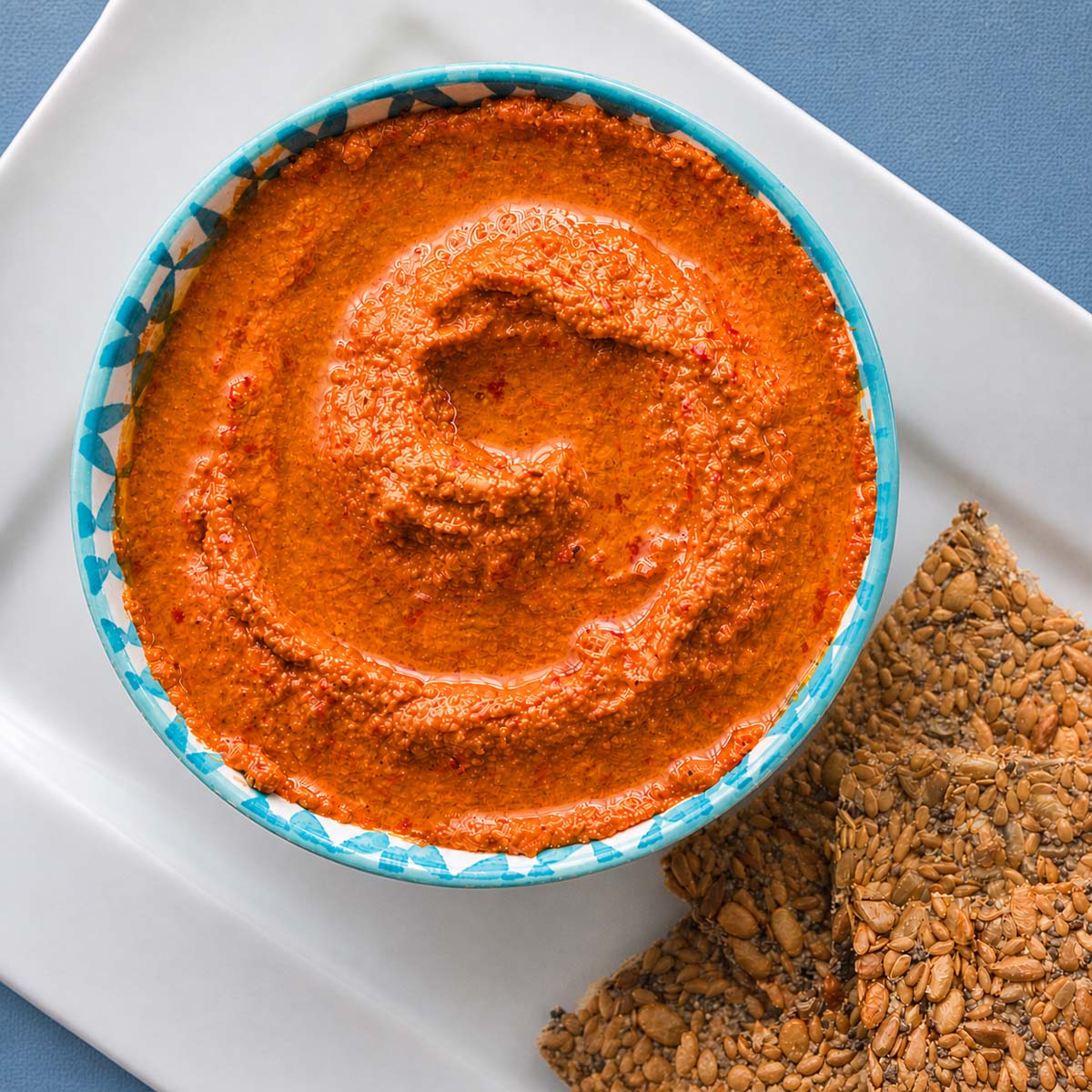Easy muhammara recipe served in a bowl with seeded crackers on a white plate