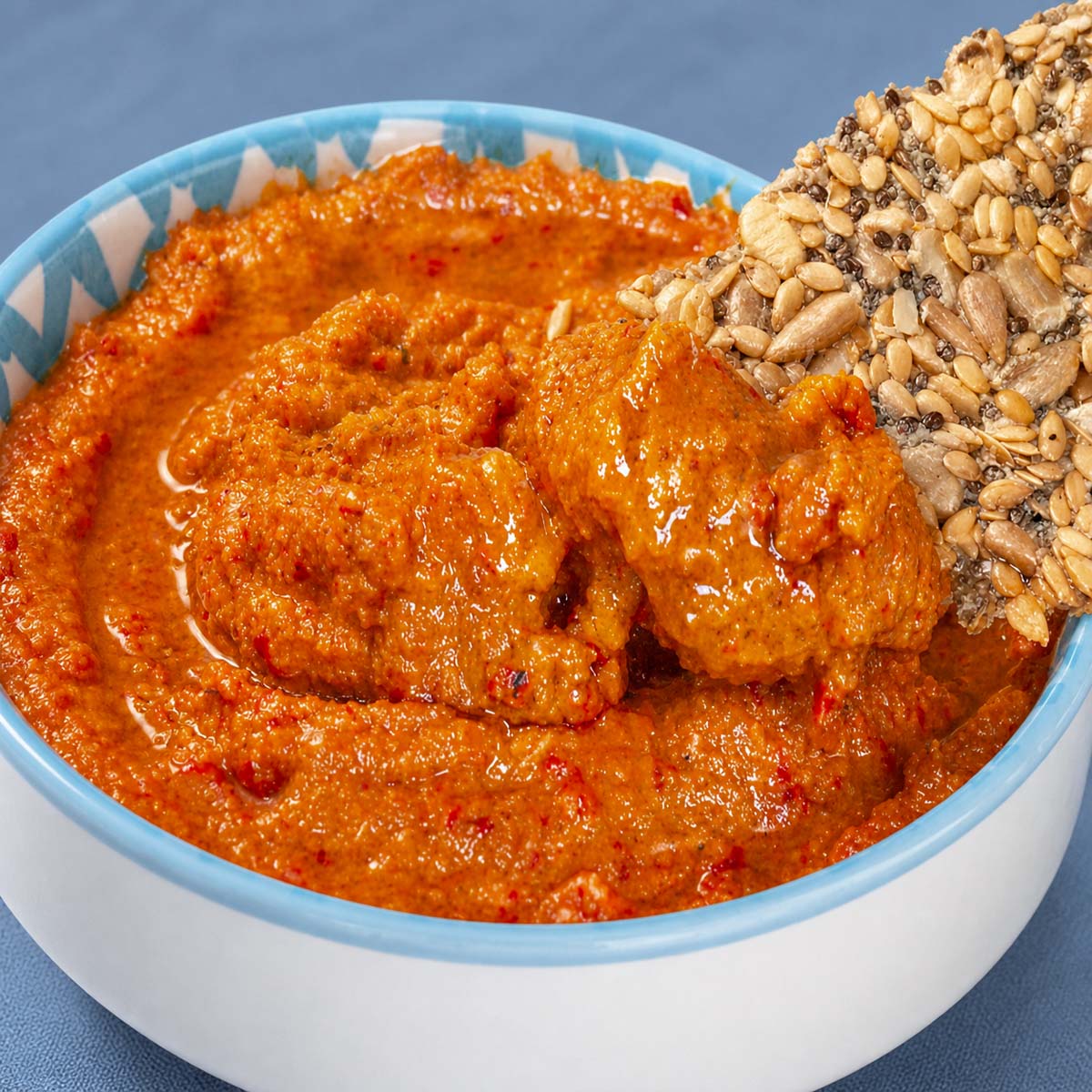 Easy muhammara recipe in a bowl with seeded crackers