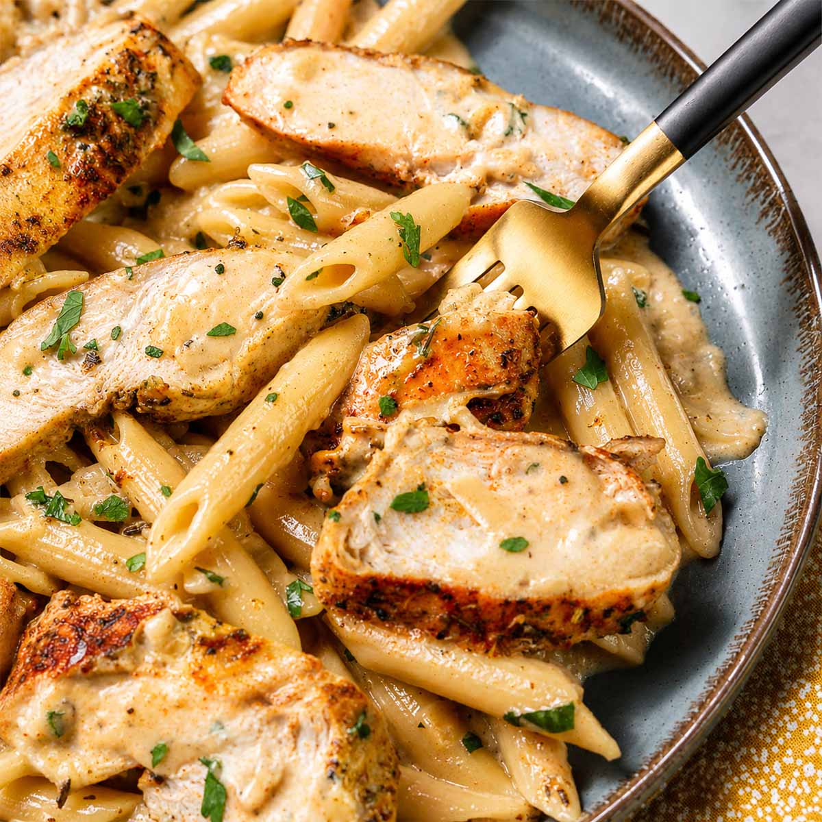 Close up One-Pan Creamy Garlic Parmesan Chicken Pasta Recipe served in a ceramic bowl with golden seared chicken, creamy parmesan sauce, and tender penne pasta.