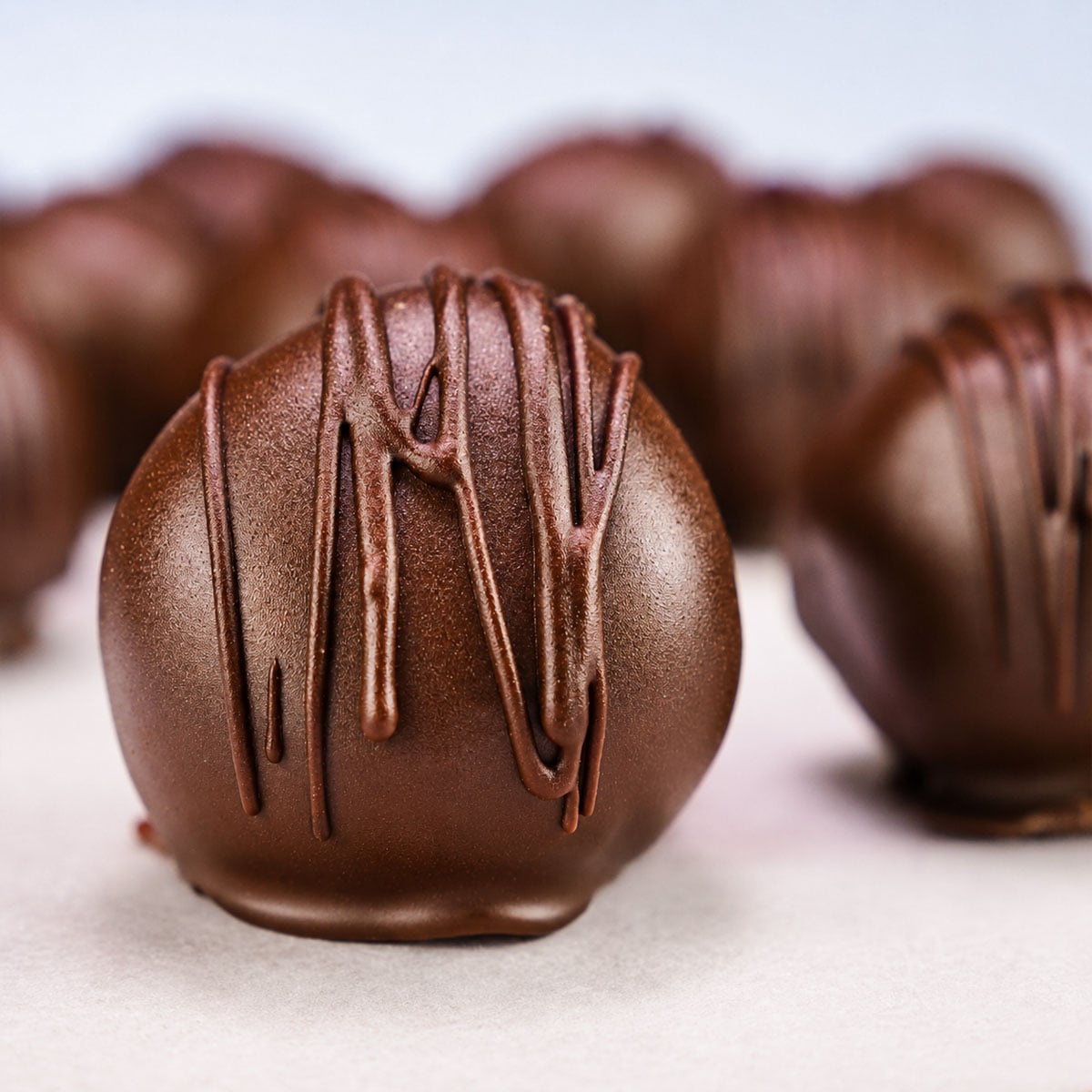 Close-up of a dark chocolate–coated peanut butter ball with chocolate drizzle on parchment paper.