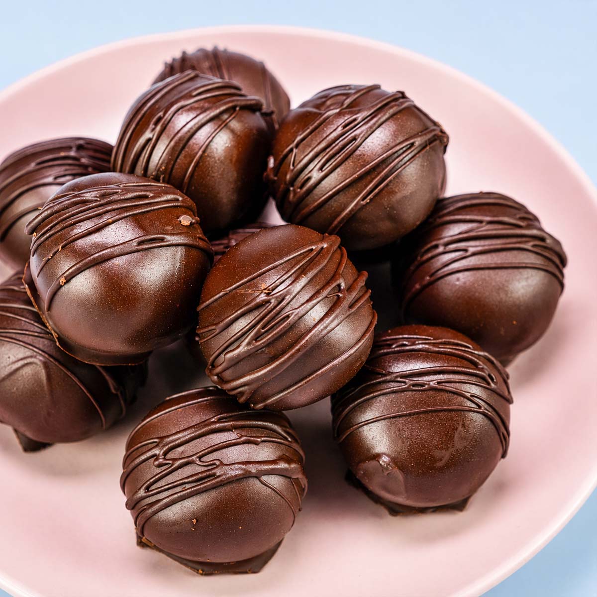 Plate of dark chocolate–coated peanut butter balls drizzled with chocolate.