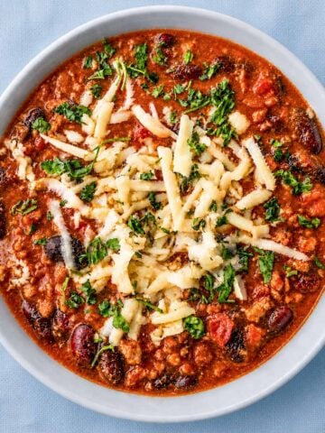 easy homemade chili with beans topped with grated cheese and fresh herbs in a white bowl