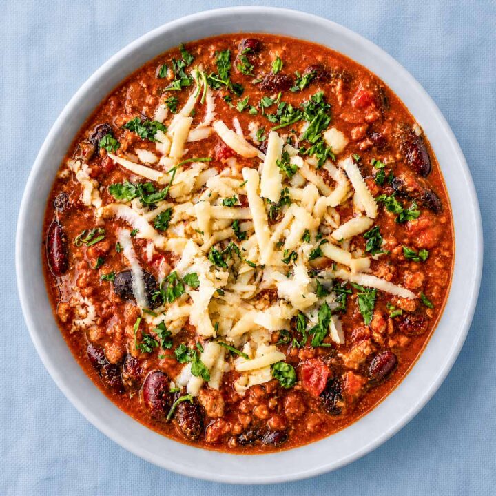 easy homemade chili with beans topped with grated cheese and fresh herbs in a white bowl