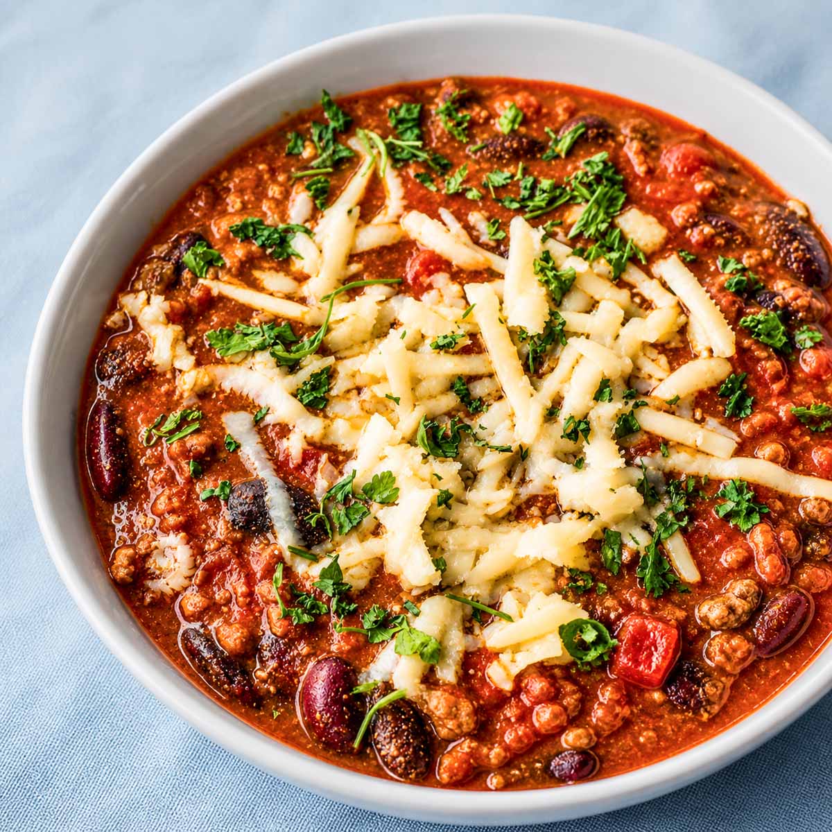 easy pork chili with beans, grated cheese, and fresh herbs in a white bowl