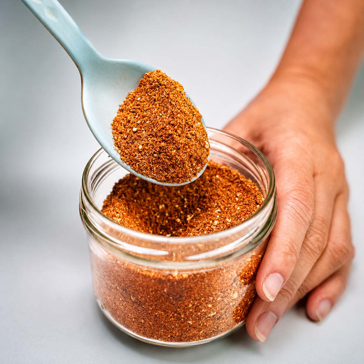 Close-up of homemade pork chop seasoning in a glass jar with a spoonful of spice blend
