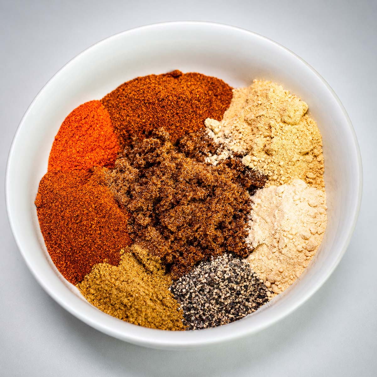 Ingredients for pork chop seasoning in a white bowl with paprika, brown sugar, garlic powder, and spices