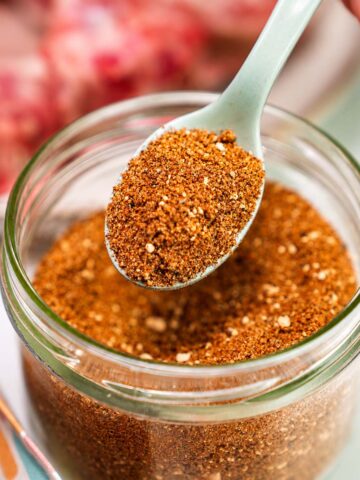 close up Pork chop seasoning in a glass jar with spoon beside raw pork chops on a plate