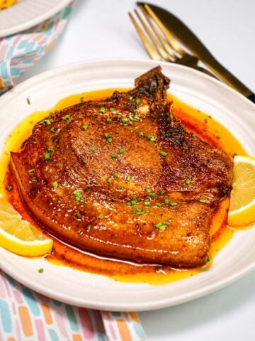 Juicy Baked Pork Loin Chops served with lemon wedges and rich buttery pan sauce on a white plate