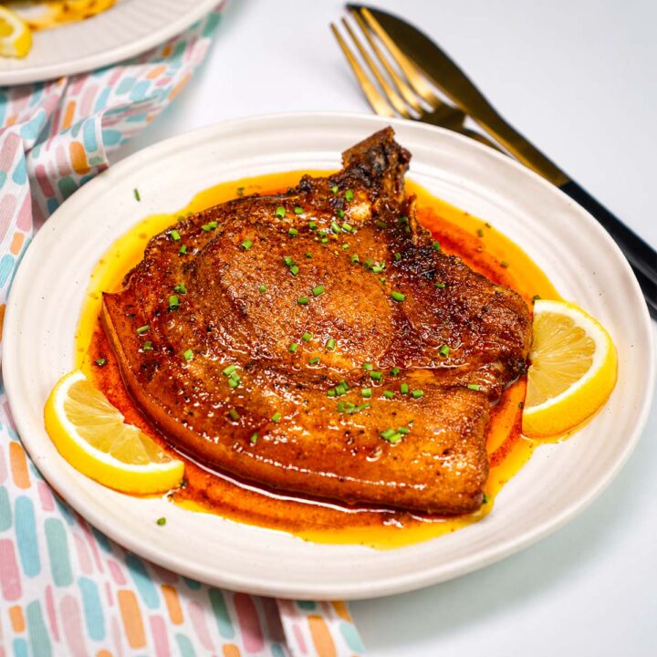 Juicy Baked Pork Loin Chops served with lemon wedges and rich buttery pan sauce on a white plate