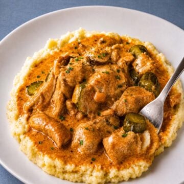Creamy pork stroganoff with mushrooms and pickles over mashed potatoes with a spoon in rich paprika sauce