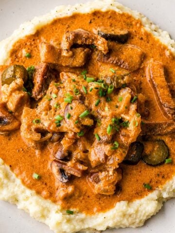 Creamy pork stroganoff served over mashed potatoes with mushrooms and pickles in a rich sauce