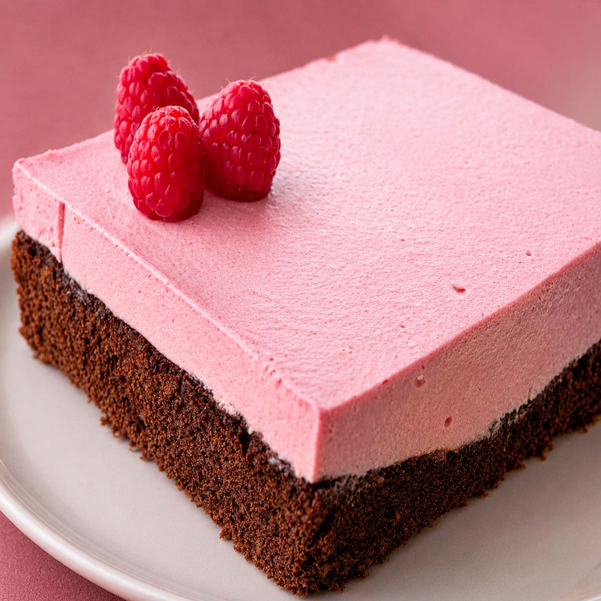 Delicate raspberry mousse chocolate cake with a rich chocolate base and fresh raspberries on top, served on a white plate