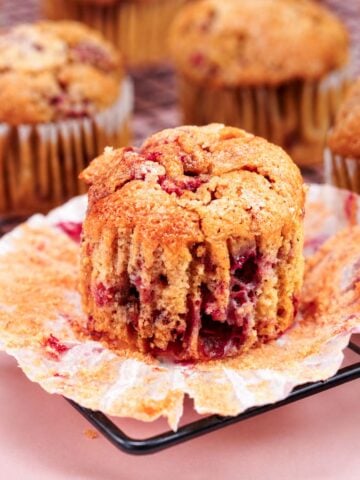 Raspberry muffins with a soft berry-filled center and golden tops cooling on a wire rack with opened muffin liner underneath