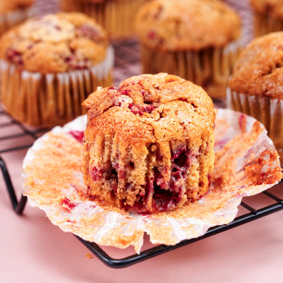 Raspberry muffins with a soft berry-filled center and golden tops cooling on a wire rack with opened muffin liner underneath