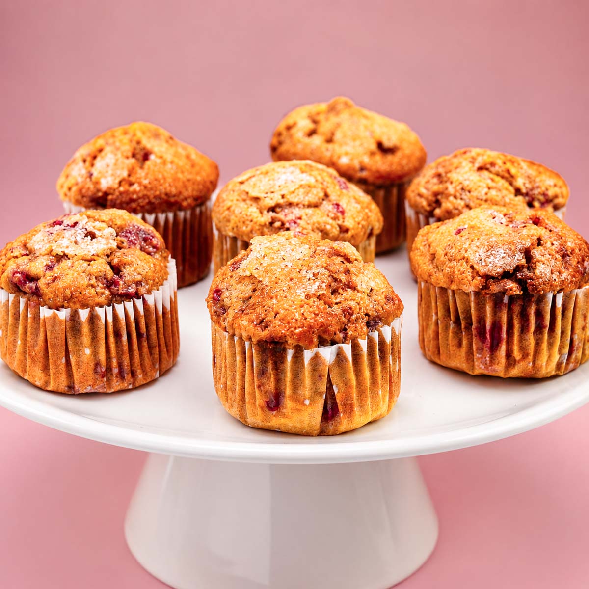Raspberry muffins on a white cake stand with golden domed tops and juicy berry pieces