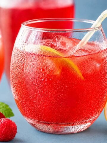 Refreshing raspberry pink lemonade served over ice in a chilled glass with fresh raspberries, lemon slices