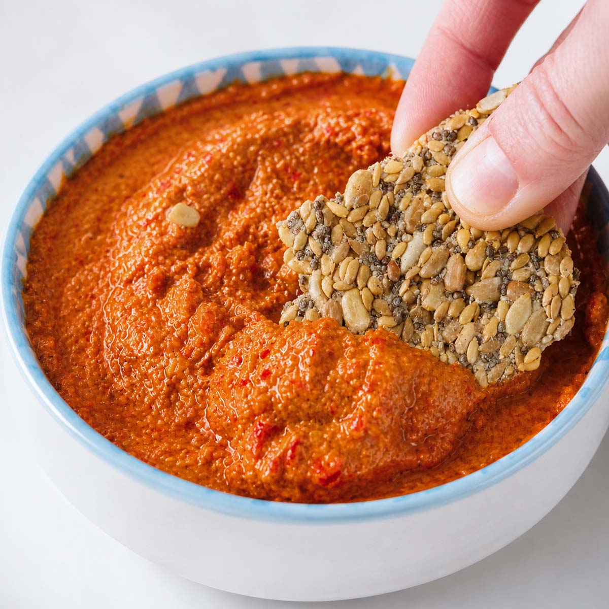 seed crackers dipping into roasted red pepper dip in a bowl