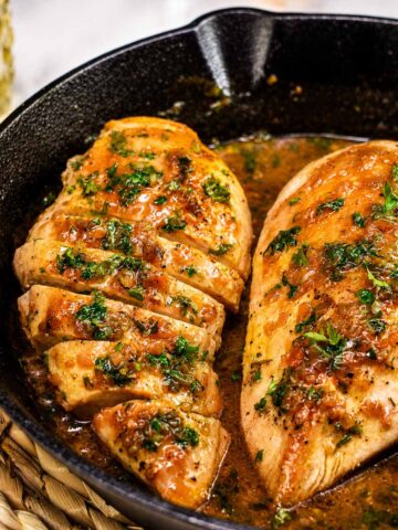 Cast iron chicken breasts in a skillet with garlic butter sauce and fresh parsley garnish