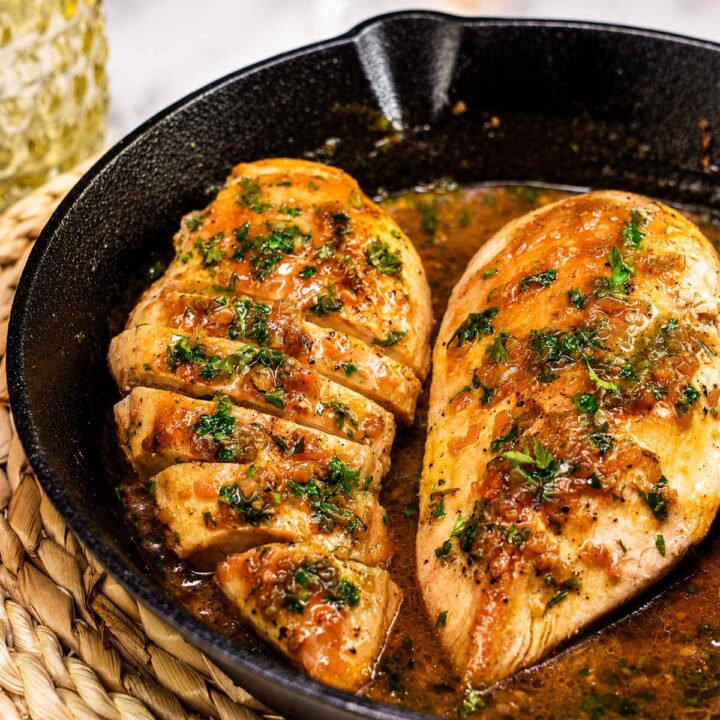 Cast iron chicken breasts in a skillet with garlic butter sauce and fresh parsley garnish