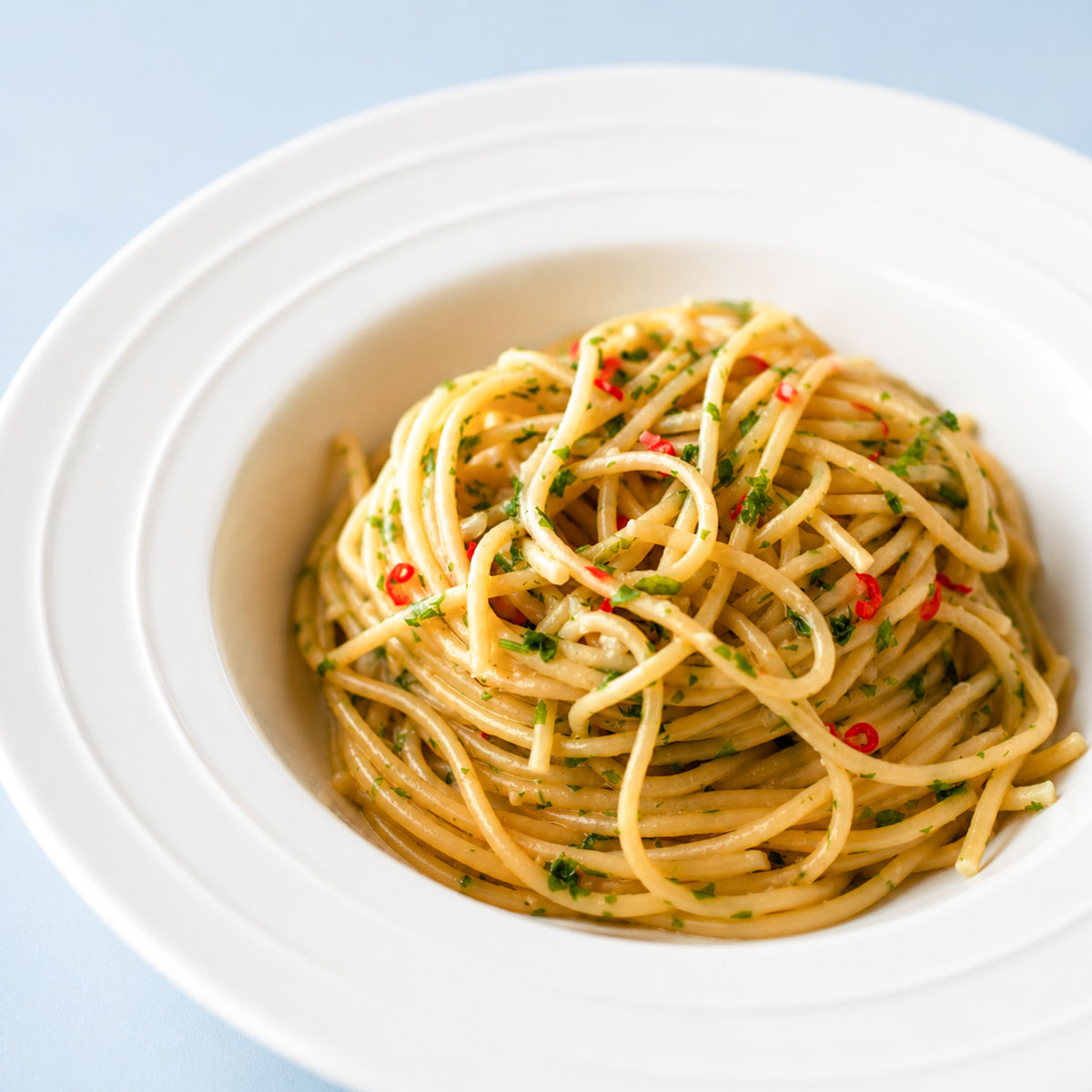 Close up Spaghetti Aglio e Olio served in a white pasta bowl, tossed with garlic olive oil, parsley, and red chili for a classic Italian pasta dish.
