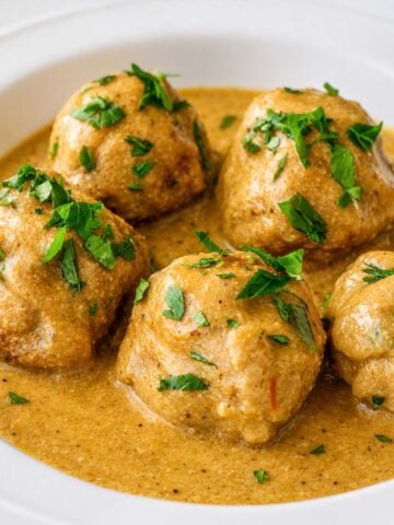 Albondigas (Spanish meatballs) simmered in a creamy almond sauce, garnished with fresh parsley and served in a white bowl.