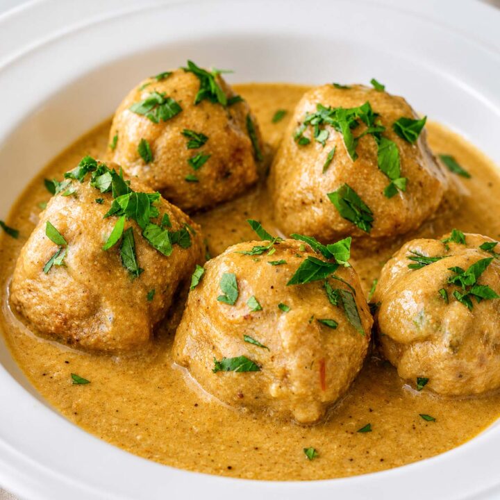 Albondigas (Spanish meatballs) simmered in a creamy almond sauce, garnished with fresh parsley and served in a white bowl.