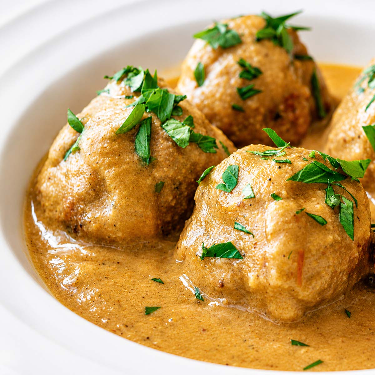 Spanish meatballs (albondigas) in a creamy almond sauce, topped with chopped parsley and served in a white bowl.