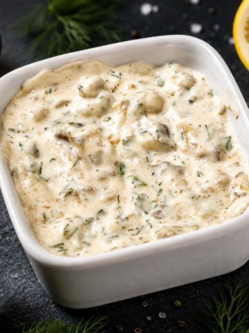 Homemade Tartar Sauce in a white bowl with pickles, lemon, and fresh herbs