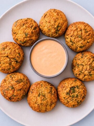 Crispy tuna and potato patties served with a creamy dipping sauce on a white plate.