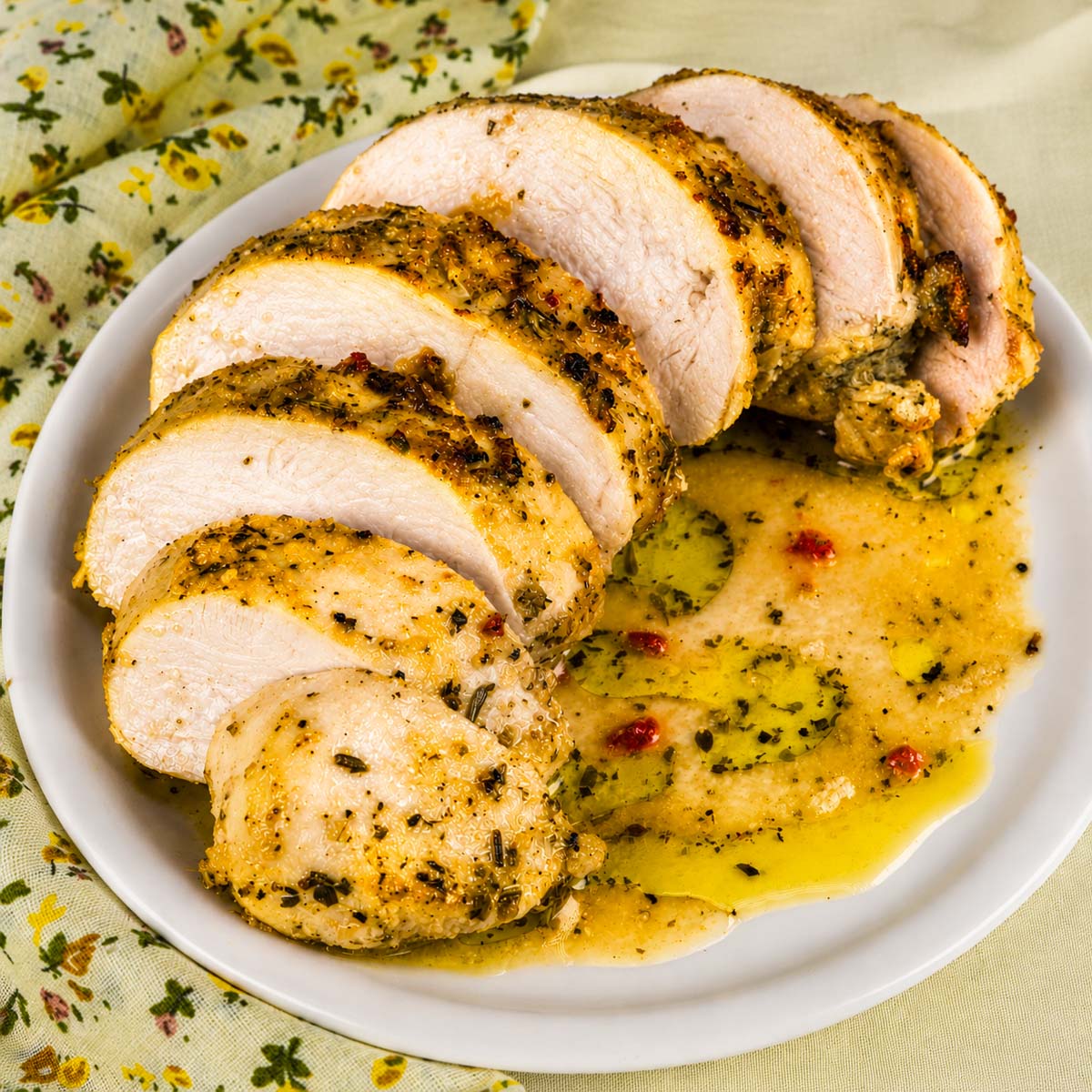 Sliced Italian dressing chicken breast fanned on a plate with garlicky herbed pan sauce and a sprinkle of parsley.