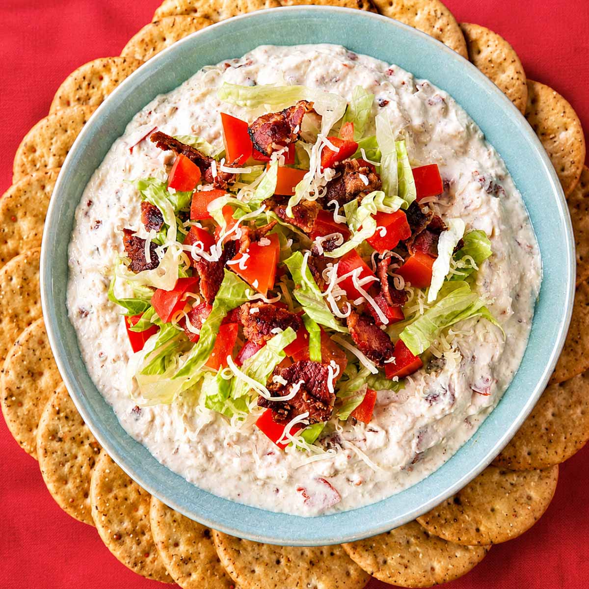 Creamy BLT dip topped with crispy bacon, diced tomatoes, shredded romaine, and cheddar, served with crackers.