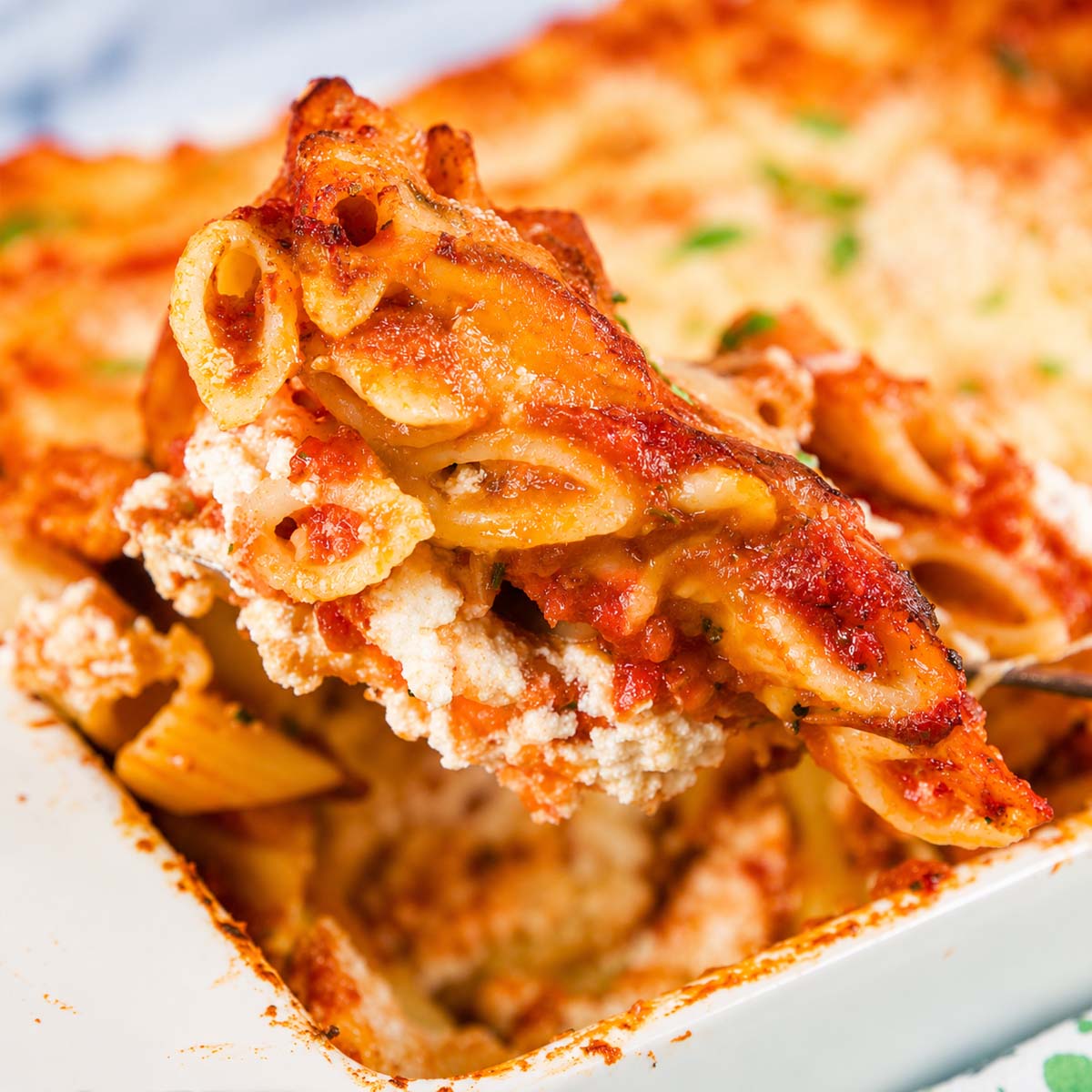 Close-up of Baked Ziti with Ricotta and Mozzarella lifted from a baking dish, showing cheesy pasta layers and marinara sauce