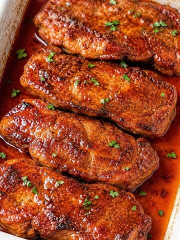 Baked pork steaks in a rich reddish sauce, garnished with chopped parsley and cooked until tender in the oven.