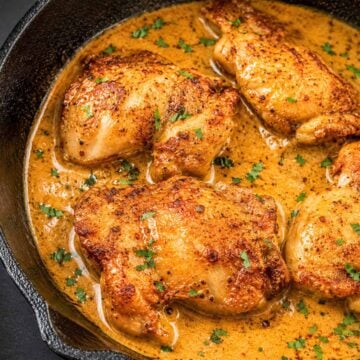 Boneless skinless chicken thighs seared until golden in a cast-iron skillet, simmering in a creamy pan sauce and topped with chopped parsley.